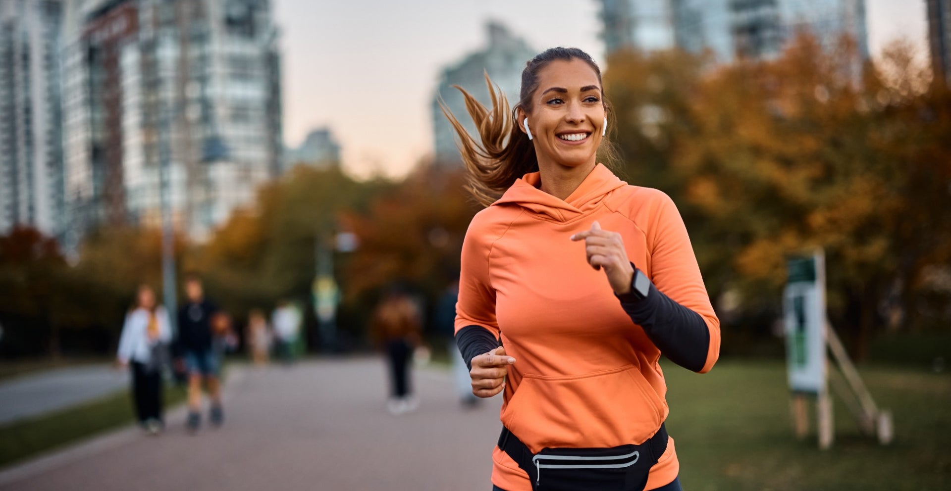 Happy sportswoman wearing an orange sweatshirt with earbuds running in park